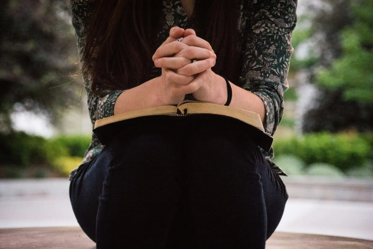 A woman sitting on the ground with her hands folded together.