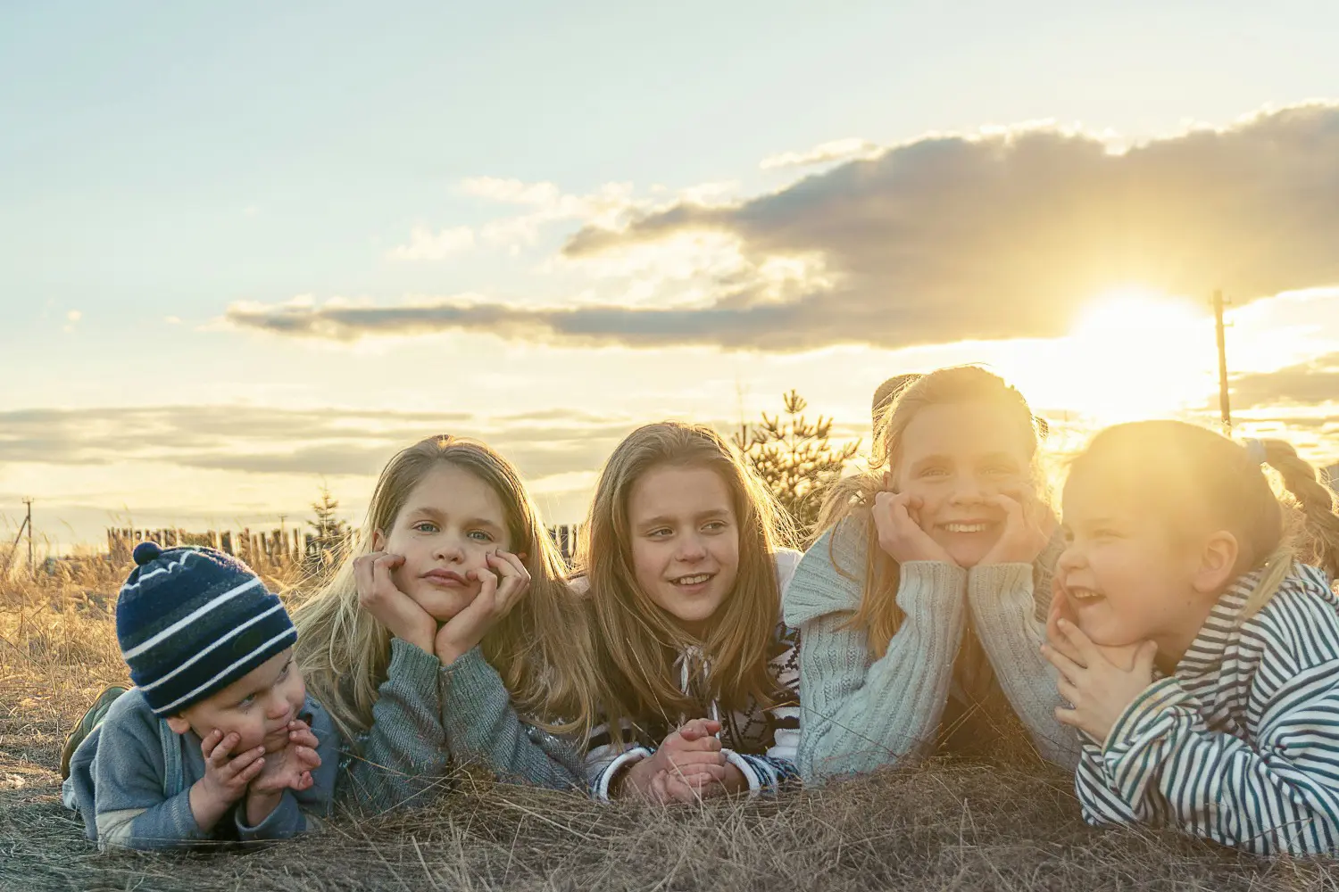 A group of people laying in the grass with their hands on their heads.