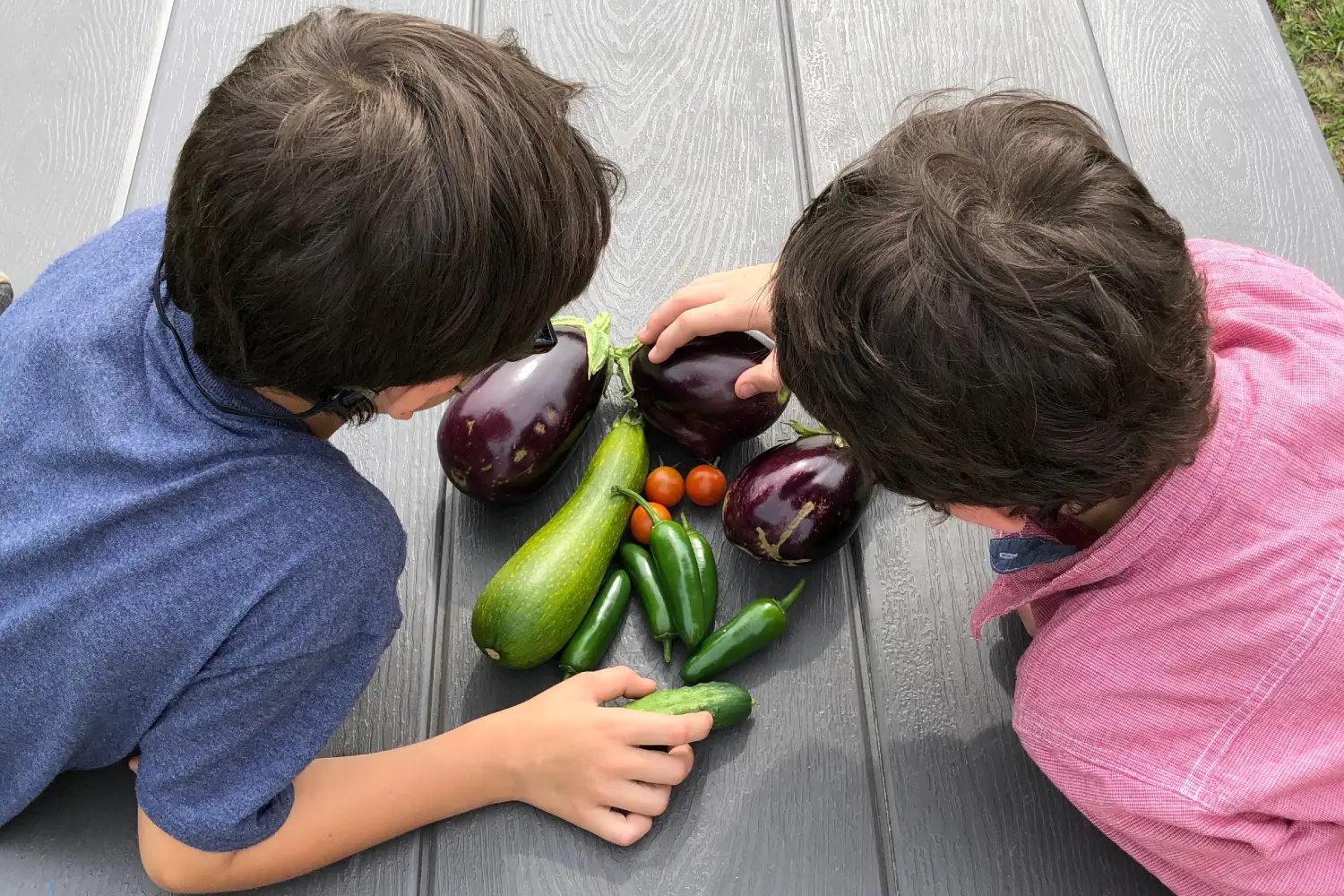 Two children sitting on the ground with a variety of vegetables.