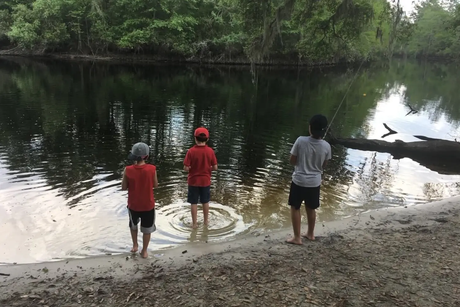 Three kids standing in the water with a fishing rod.